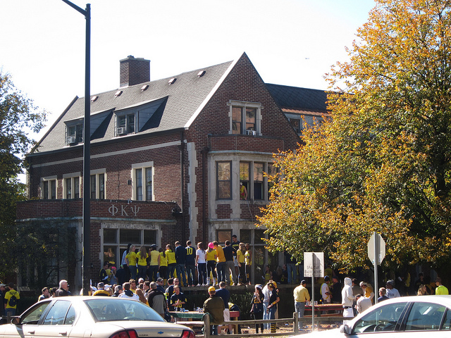 College girls wearing yellow shirts standing outside of a sorrority house.