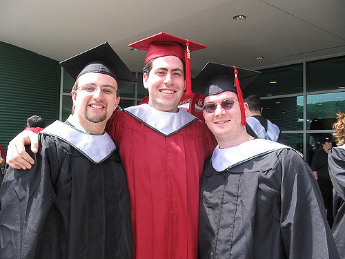 Three peopole wearing graduation robes standing arm in arm.