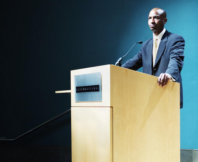A man in a suite and tie standing behind a podium with a microphone.