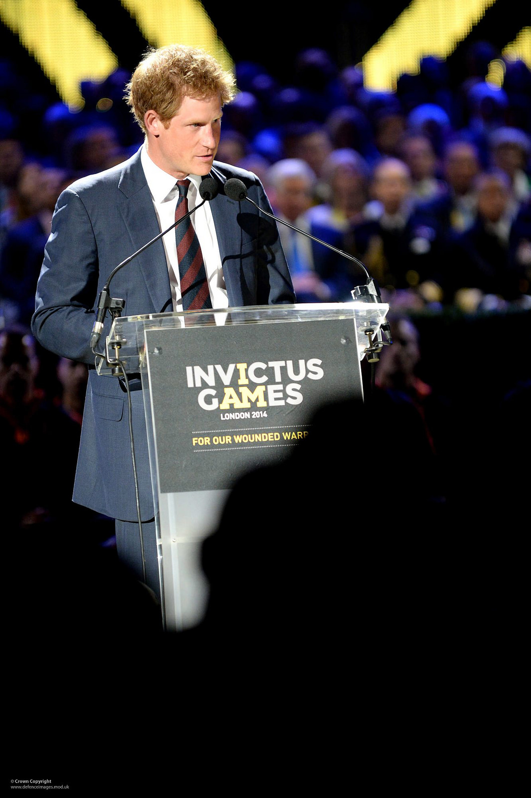 Prince Harry speaking at a podium with the sign "Invictus Games London 2014 for our wounded warriors."