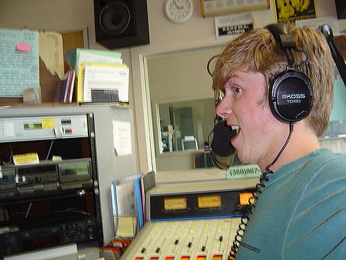 A young man wearing headphones in a radio studio and talking into a microphone.