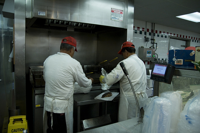 Two people preparing food on a grill at a fast food restaurant.