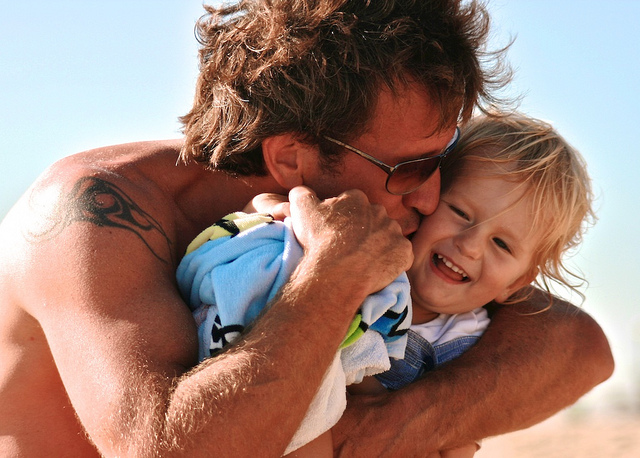 A father hugging and kissing a toddler.
