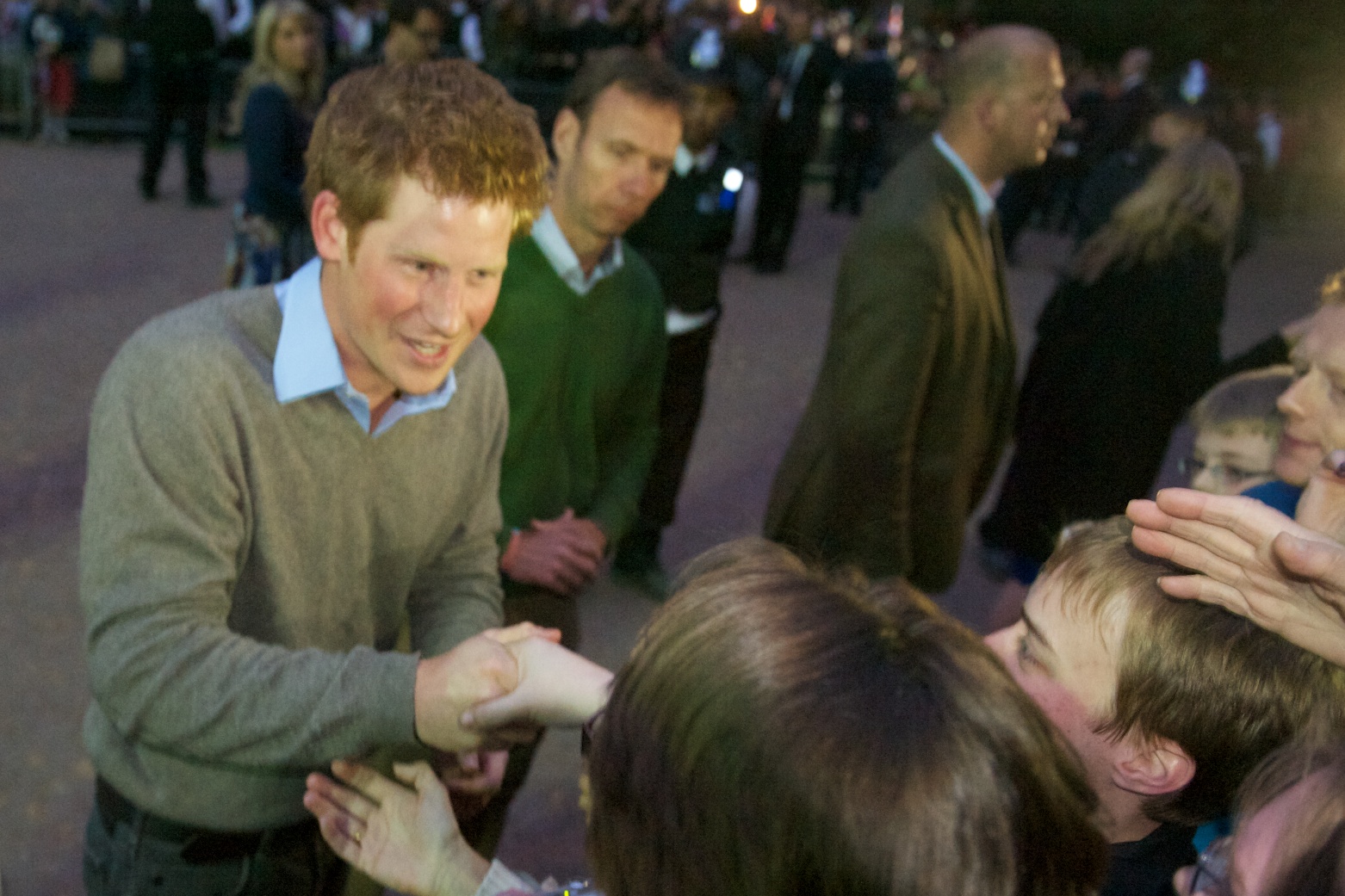A younger Prince Harry smiling and shaking hands with someone in a crowd.