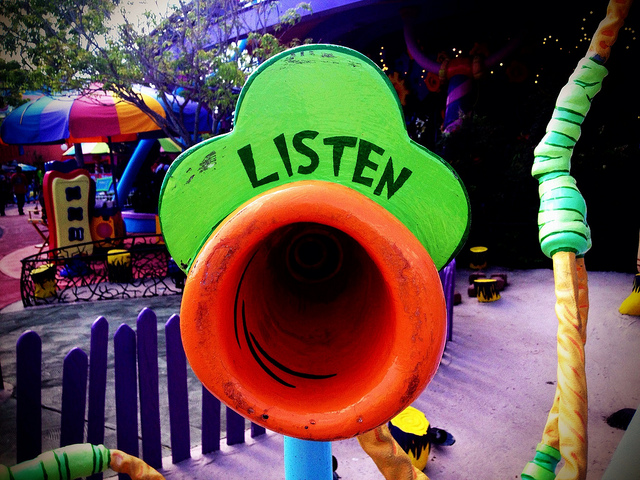 A whimsical green and orange listening device with "LISTEN" written on it in a colorful outdoor setting.