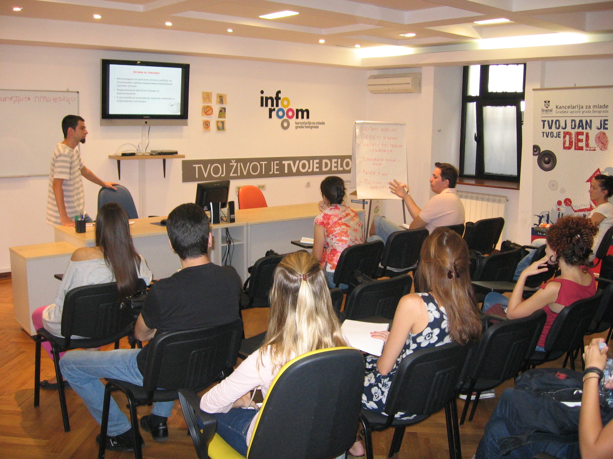 A small classroom with people seated in chairs and a speaker in front.