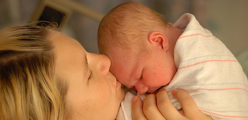 A mother kissing the forehead of her newborn baby.