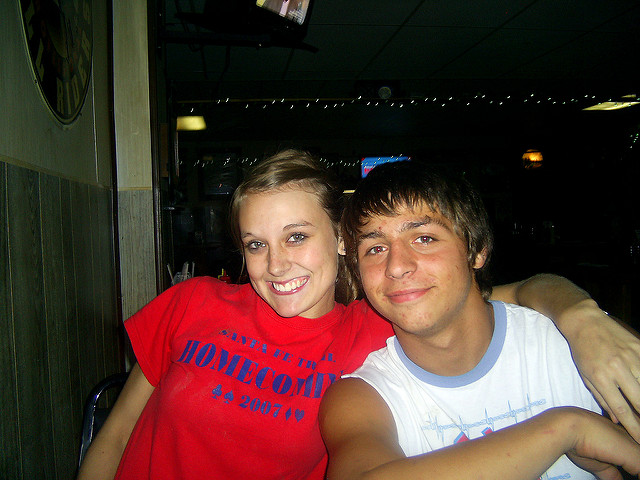 A young woman putting her arm around a young man, looking like friends.