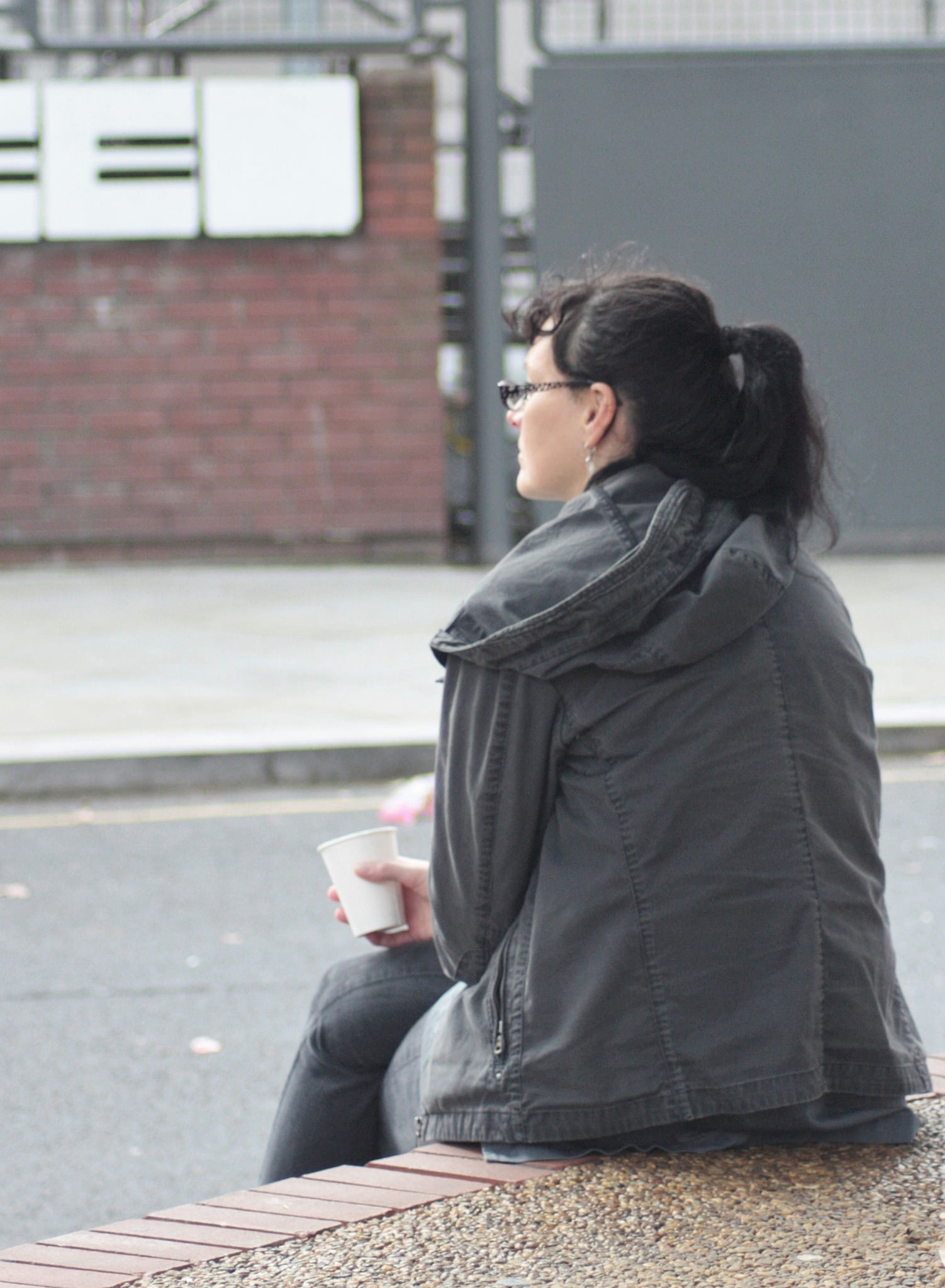 A young woman sitting by herself outside looking away from the camera.