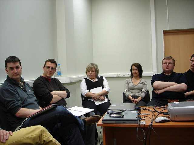 A group of co-workers sitting around a desk with everyone looking at something off screen.