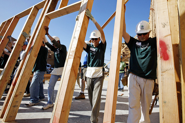 Several people wearing hardhats working together outside to frame a building structure.