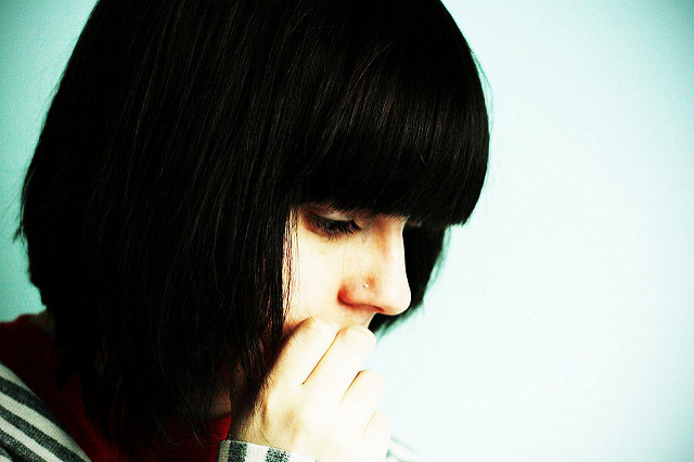 A woman expressing anxiety by looking down and biting her nail.