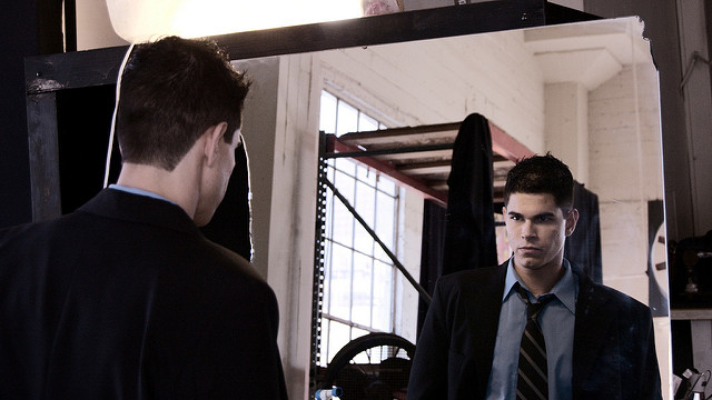 A young man in a suite and tie practicing his speech in front of a mirror.