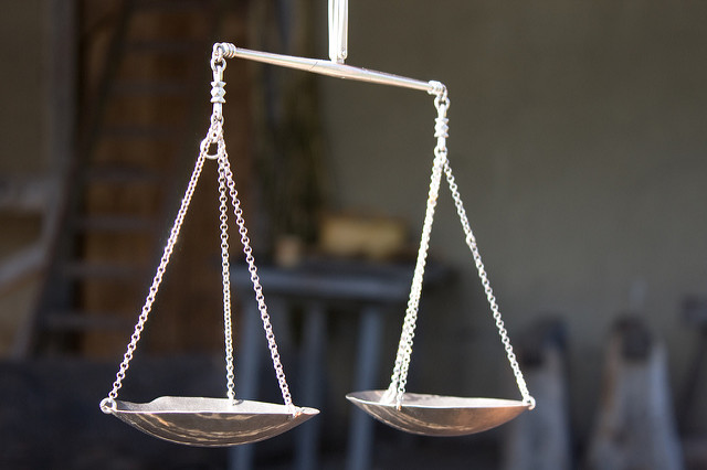 Close-up of a traditional balance scale with two metal pans hanging from a beam.