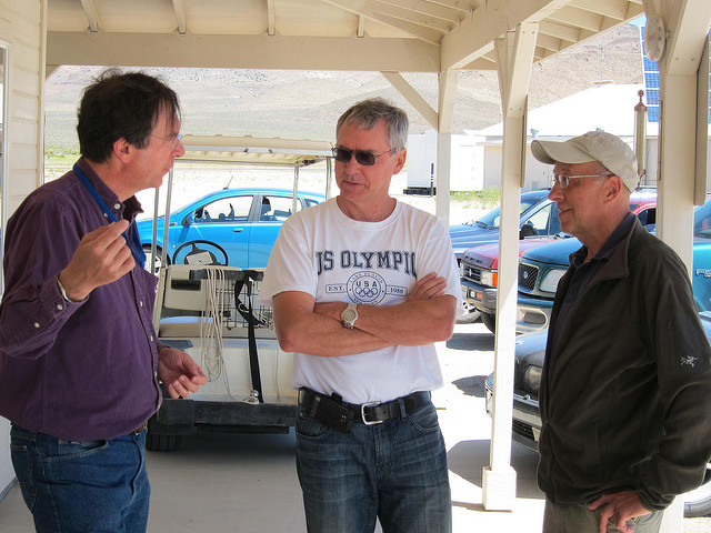 One coworker talking to two fellow coworkers outside under a canopy.