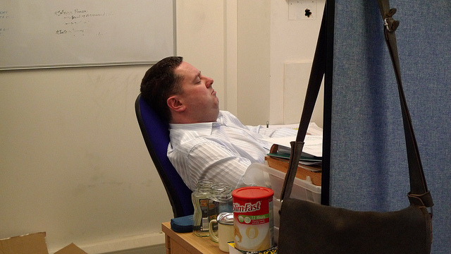 A man sleeping in an office chair behind a cubicle.