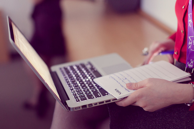 A laptop on a woman's lap with a notepad in her hand.