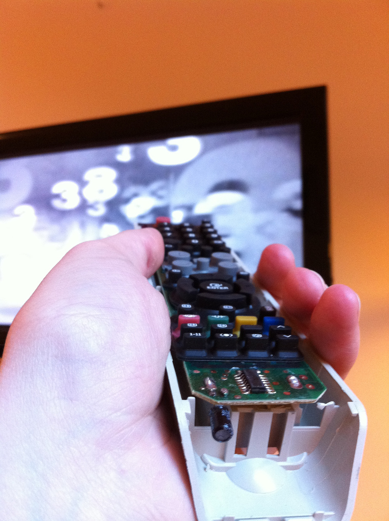 A hand holding a remote control pointed at a television.
