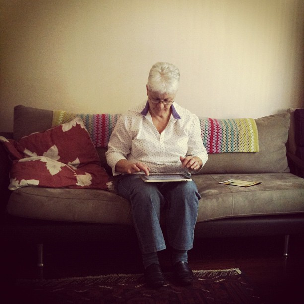 An older woman sitting on the couch using a tablet.