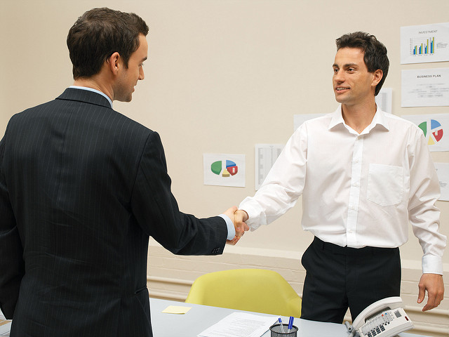 Two people shaking hands over an office desk.