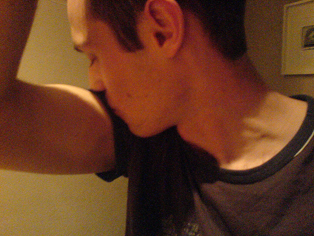 A young man with raised arm and head turned to the side smelling his armpit.