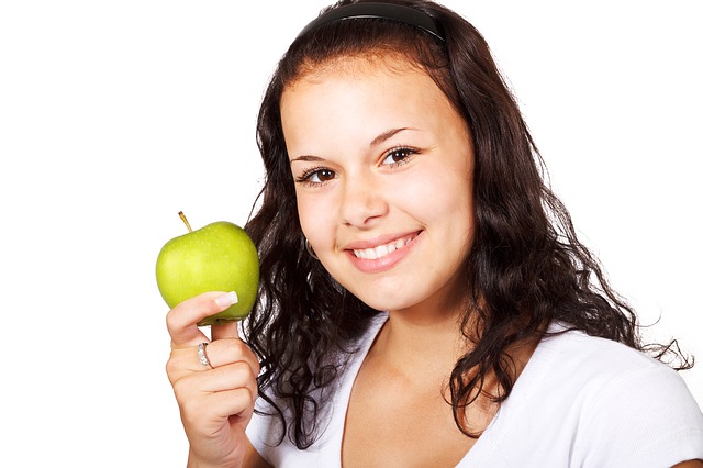 A young woman holding an apple and smiling.