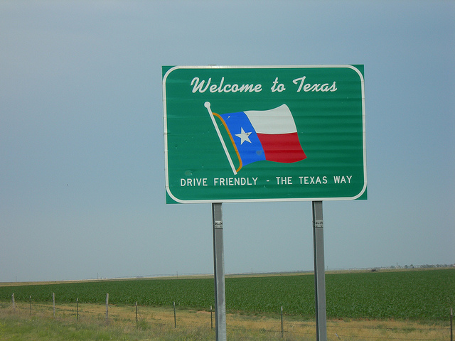 A green highway sign with Texas flag saying "Welcome to Texas, drive friendly - the Texas way."