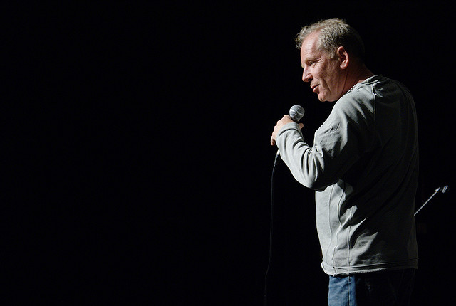 A man standing with a microphone on dark stage.