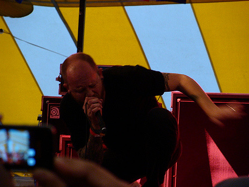 A man performing on stage under a yellow and blue tent, holding a microphone.