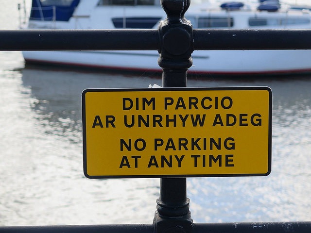 A yellow road sign indicating "no parking at anytime" in Welsh and English.
