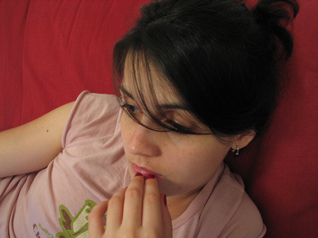 A woman sitting down looking into the distance with a neutral expression and slouching in her seat.
