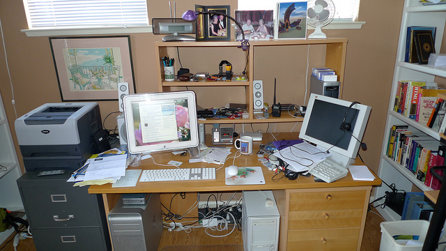 A messy desk with computer monitors, cords and papers strewn about.