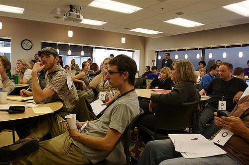 People listening to someone talk showing varying levels of engagnement, with some looking at phones, others at the floor and some at the speaker.
