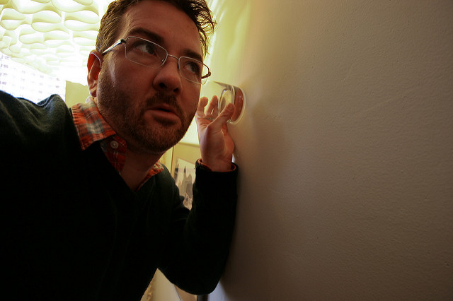 A man holding glass to his ear and to the wall.