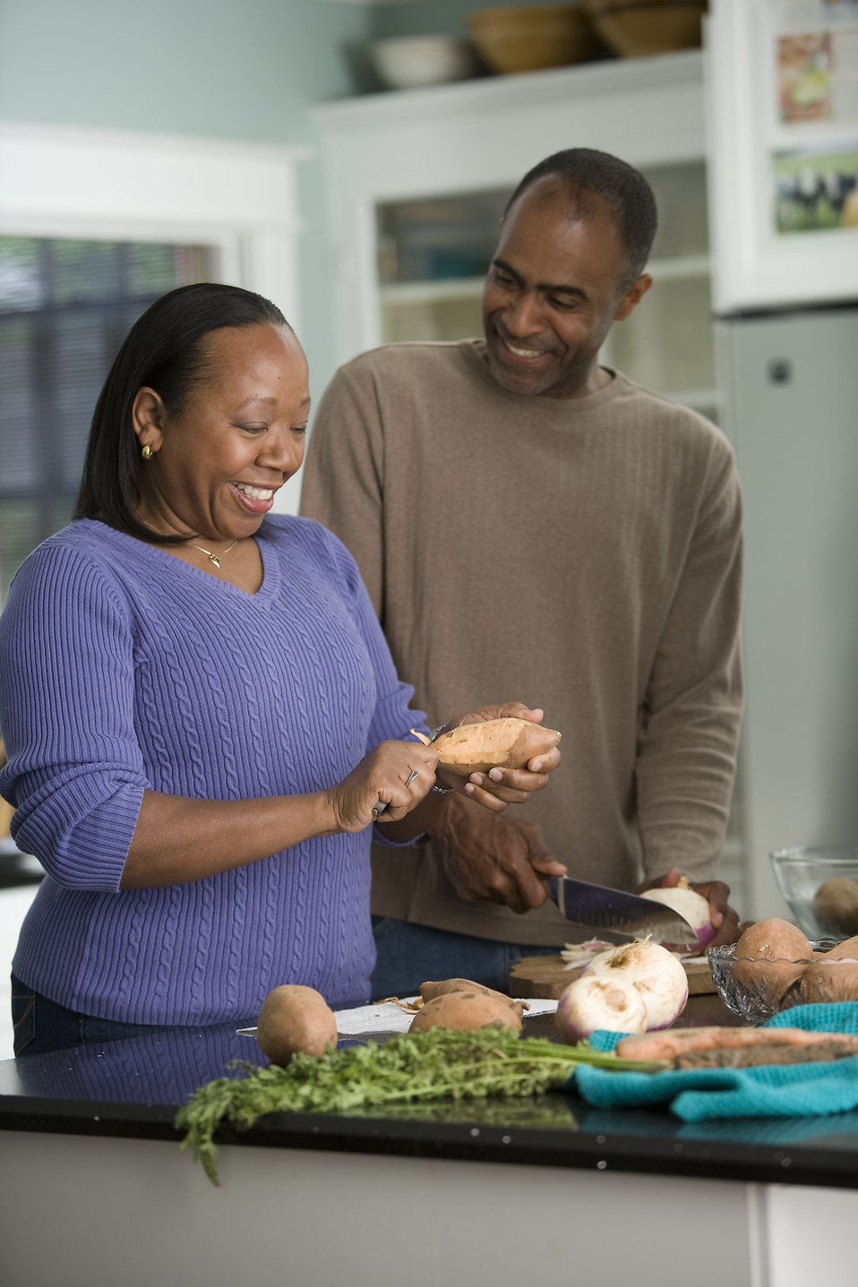 Two people in a kitchen smiling and preparing food together.