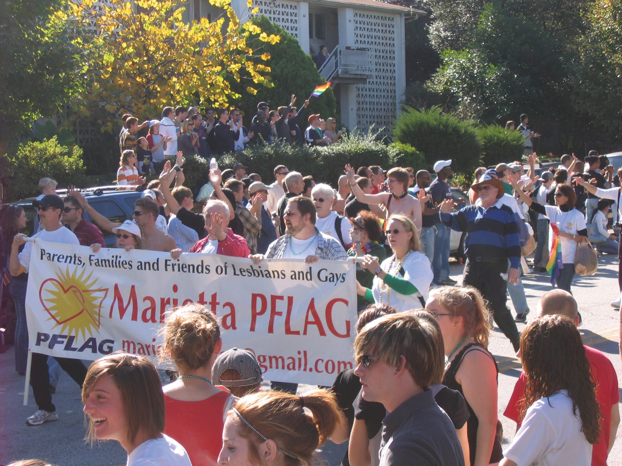 People marching in a street holding a sign that says "Parents, Families and Friends of Lesbians and Gays, Marietta PFLAG."