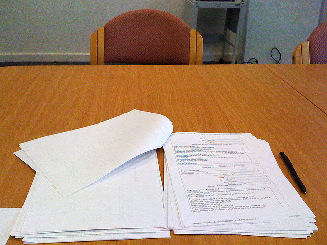 A stack of papers and pen on a table.