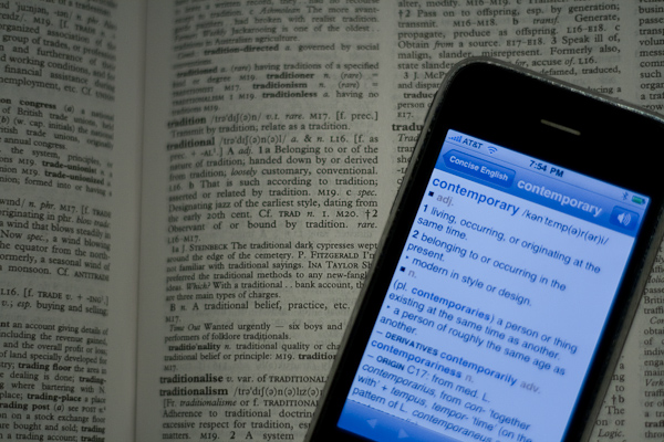 An open dictionary with a smartphone displaying the entry for "contemporary."