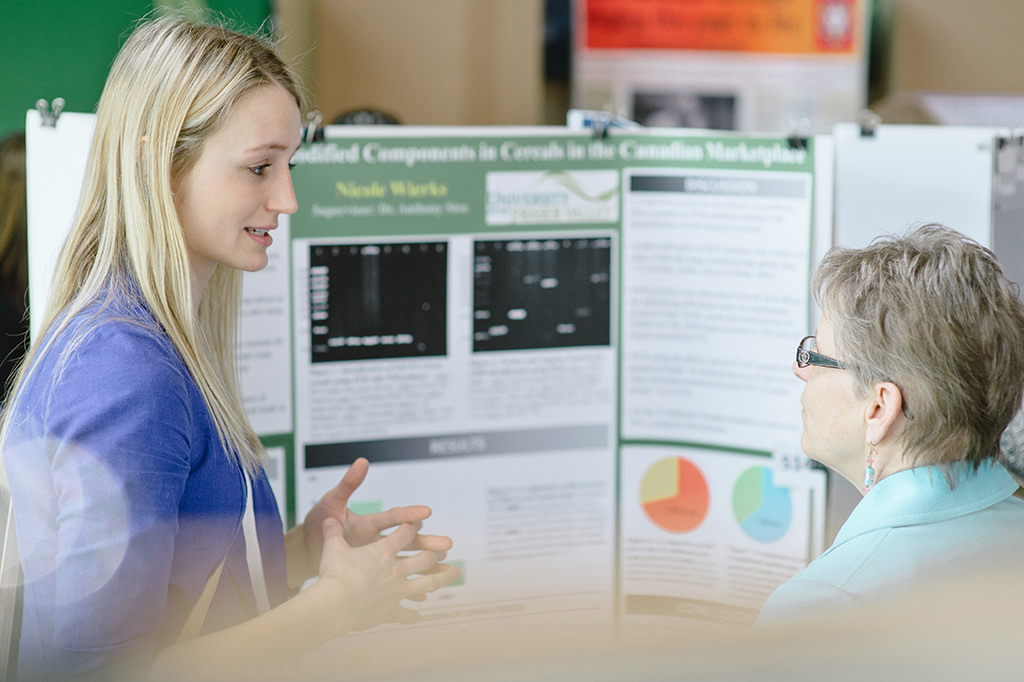 A woman speaking to another woman in front of printed poster board display.