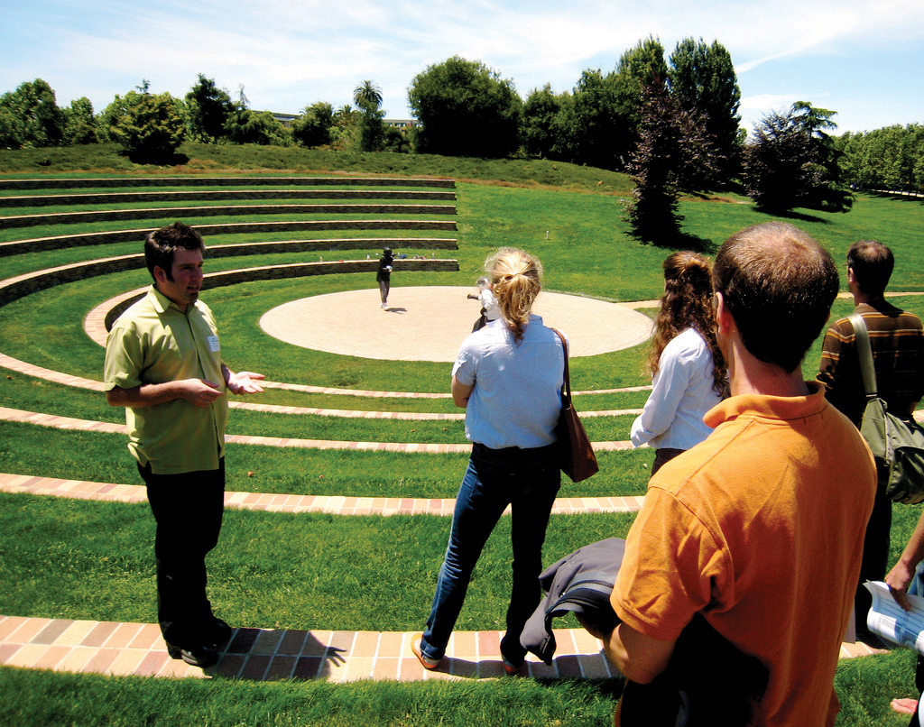 A small outside grassy stadium with four people listening to tour guide.